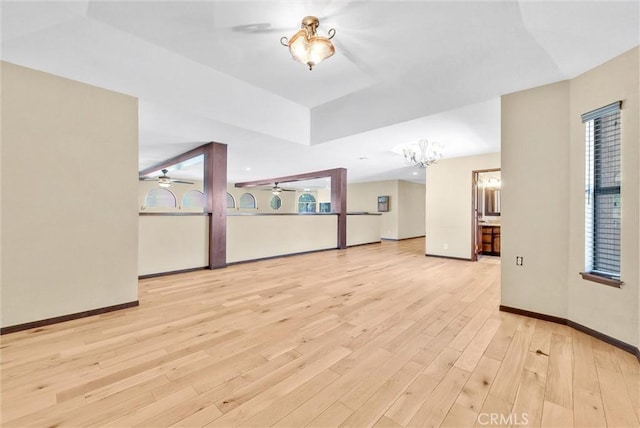 unfurnished living room featuring ceiling fan with notable chandelier and light hardwood / wood-style floors