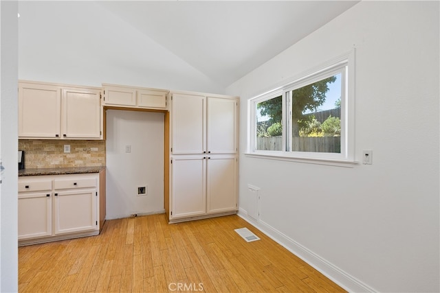 kitchen with lofted ceiling, tasteful backsplash, dark stone counters, and light hardwood / wood-style flooring