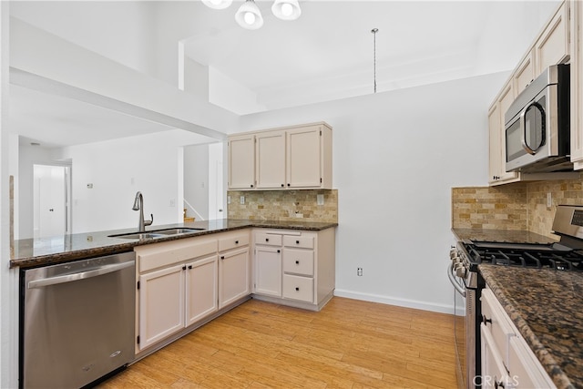 kitchen with dark stone counters, light hardwood / wood-style floors, tasteful backsplash, sink, and stainless steel appliances