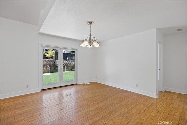 empty room featuring light wood-type flooring, a textured ceiling, and an inviting chandelier