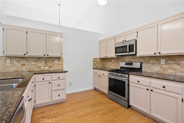 kitchen with dark stone countertops, appliances with stainless steel finishes, decorative backsplash, and light hardwood / wood-style flooring