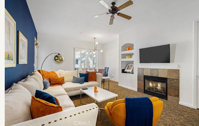 carpeted living room with built in shelves, ceiling fan with notable chandelier, and a tile fireplace