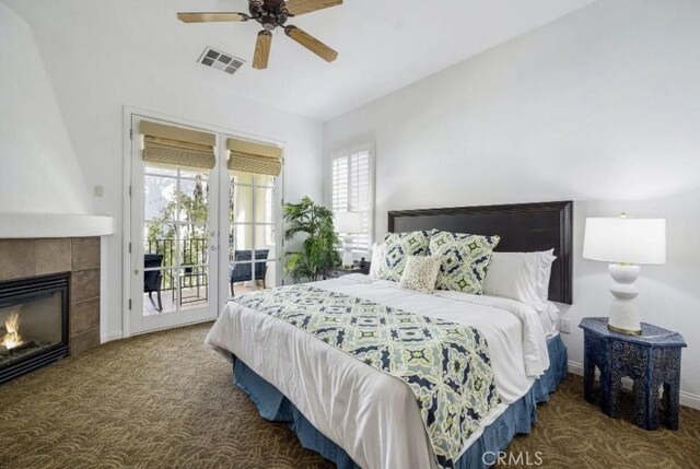 carpeted bedroom with ceiling fan, a tiled fireplace, and access to exterior