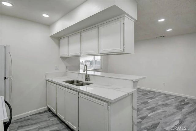 kitchen with sink, kitchen peninsula, white appliances, white cabinetry, and light stone countertops