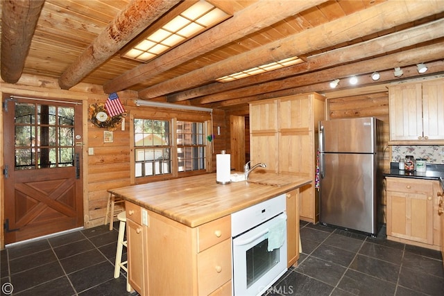 kitchen featuring light brown cabinets, oven, beam ceiling, butcher block counters, and stainless steel refrigerator