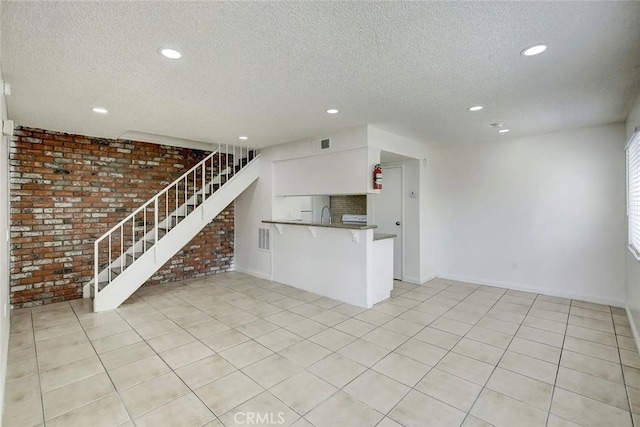 unfurnished living room with sink, light tile patterned floors, a textured ceiling, and brick wall