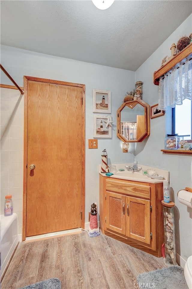 full bathroom with wood-type flooring, shower / bathtub combination, a textured ceiling, vanity, and toilet