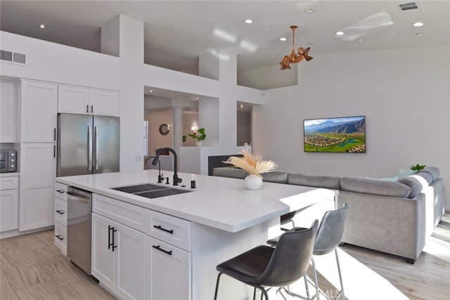 kitchen with visible vents, open floor plan, a center island with sink, appliances with stainless steel finishes, and a sink