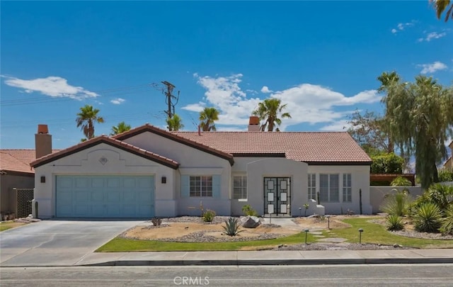 mediterranean / spanish home with stucco siding, a tile roof, concrete driveway, a garage, and a chimney