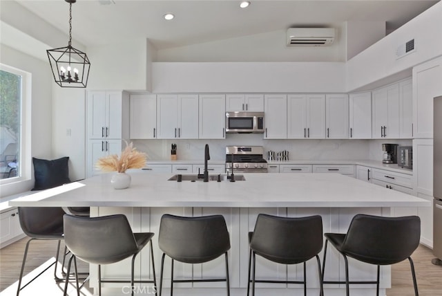 kitchen with a wall mounted AC, a sink, light countertops, white cabinets, and appliances with stainless steel finishes