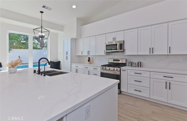 kitchen with visible vents, a sink, hanging light fixtures, white cabinets, and appliances with stainless steel finishes