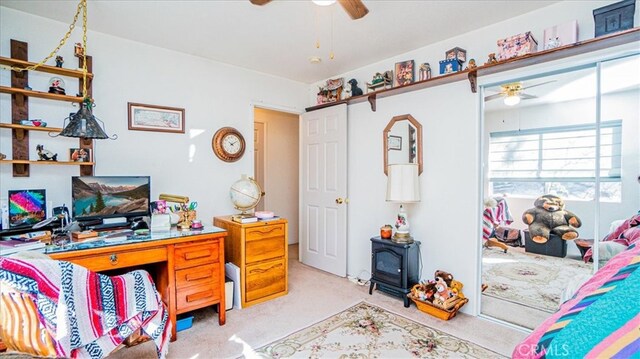 office featuring carpet flooring, a wood stove, and ceiling fan