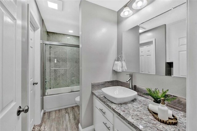 full bathroom featuring toilet, vanity, hardwood / wood-style flooring, and enclosed tub / shower combo