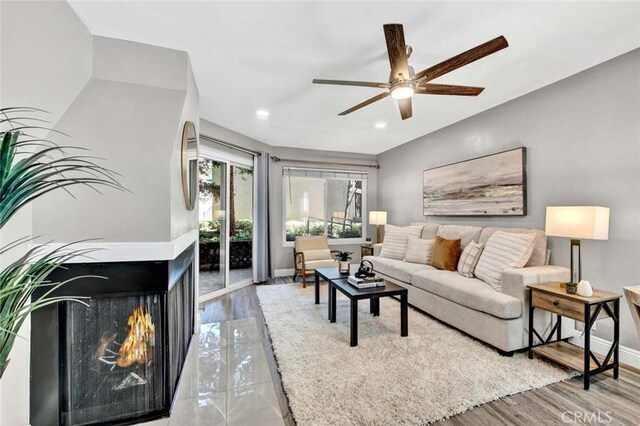 living room with ceiling fan, a multi sided fireplace, and wood-type flooring