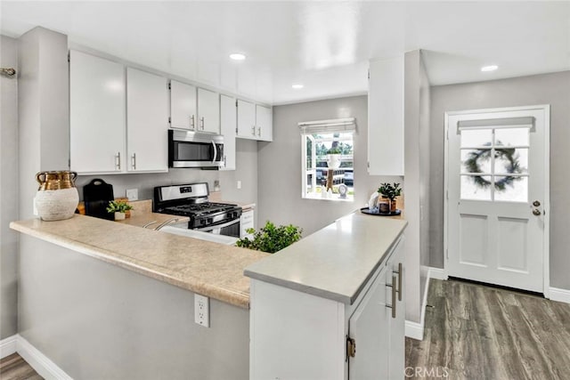 kitchen featuring hardwood / wood-style flooring, kitchen peninsula, white cabinetry, and appliances with stainless steel finishes