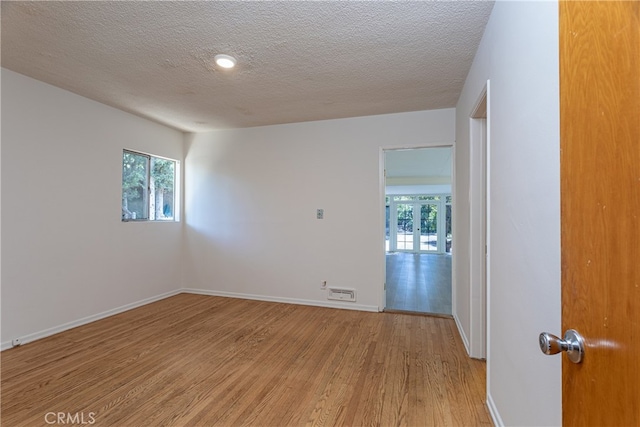 empty room with french doors, a textured ceiling, and light hardwood / wood-style flooring