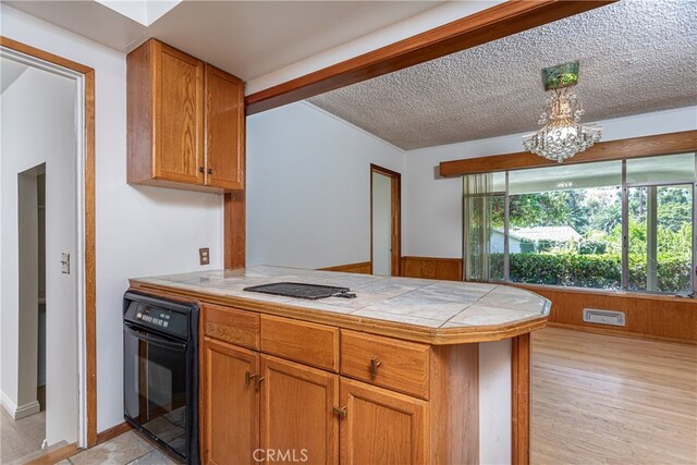 kitchen featuring light hardwood / wood-style floors, a textured ceiling, a notable chandelier, wooden walls, and black oven