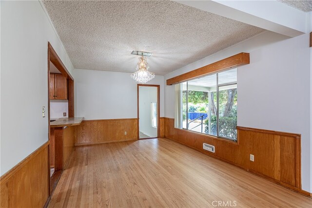 interior space featuring a textured ceiling, light hardwood / wood-style floors, wooden walls, and a chandelier