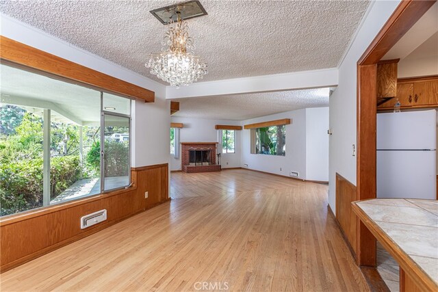 unfurnished living room with a textured ceiling, light hardwood / wood-style floors, wooden walls, and a brick fireplace