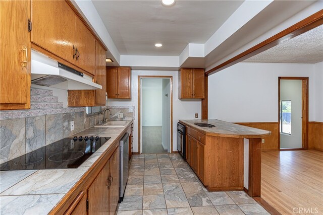 kitchen with tile countertops, black appliances, light hardwood / wood-style flooring, wooden walls, and sink