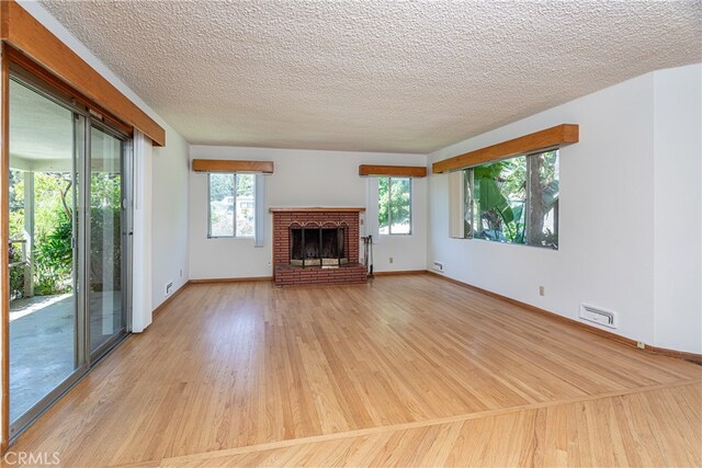 unfurnished living room featuring a brick fireplace, light wood-type flooring, and a textured ceiling