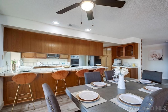 dining area featuring ceiling fan, sink, a textured ceiling, and light hardwood / wood-style floors