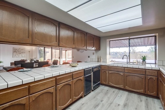 kitchen with light hardwood / wood-style flooring, sink, tile counters, and dishwasher