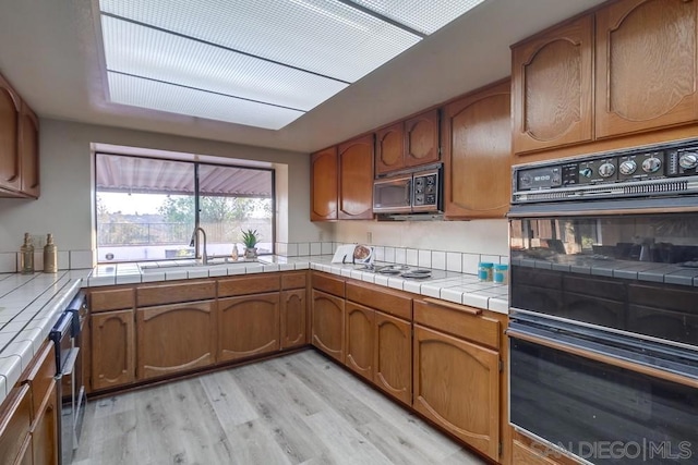 kitchen featuring black appliances, sink, tile counters, and light hardwood / wood-style floors