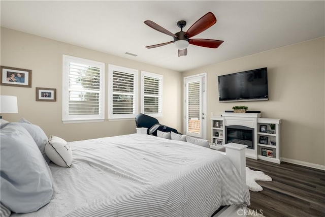 bedroom featuring ceiling fan, dark wood finished floors, visible vents, baseboards, and a glass covered fireplace