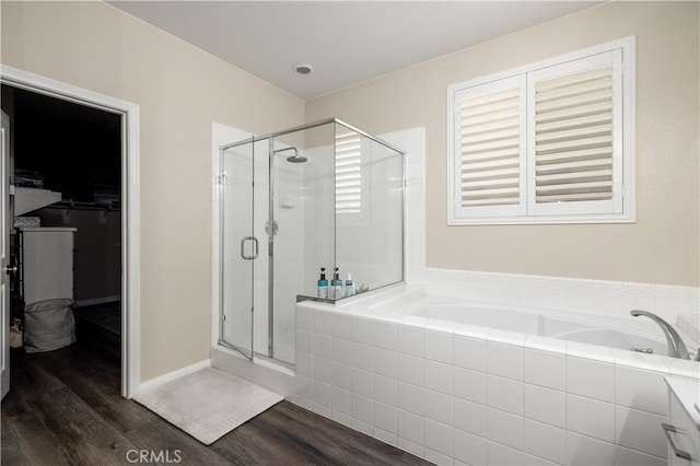 full bathroom with a spacious closet, wood finished floors, a shower stall, and a bath