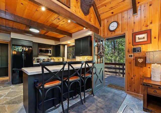 kitchen with a breakfast bar, wooden walls, wooden ceiling, black refrigerator, and kitchen peninsula