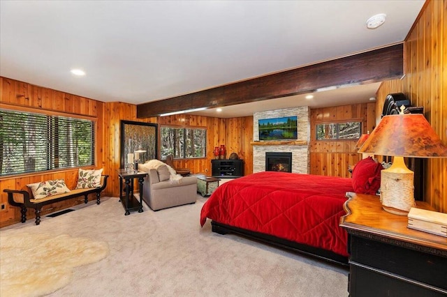 bedroom with beam ceiling, a fireplace, wood walls, and light colored carpet