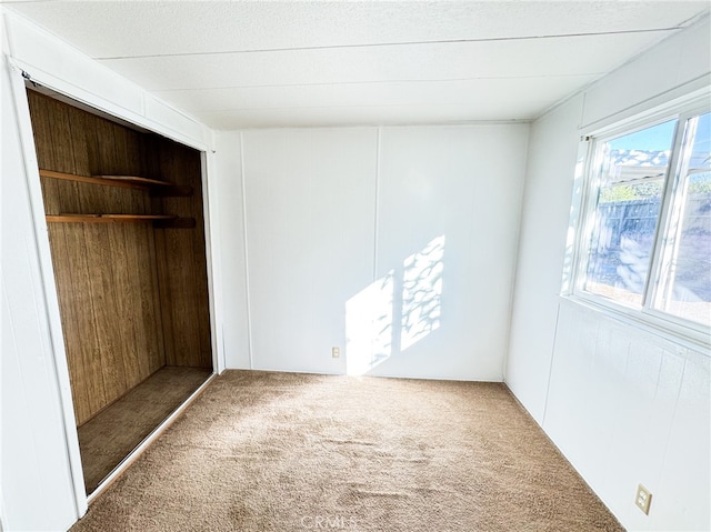 unfurnished bedroom with wooden walls, carpet flooring, and a closet