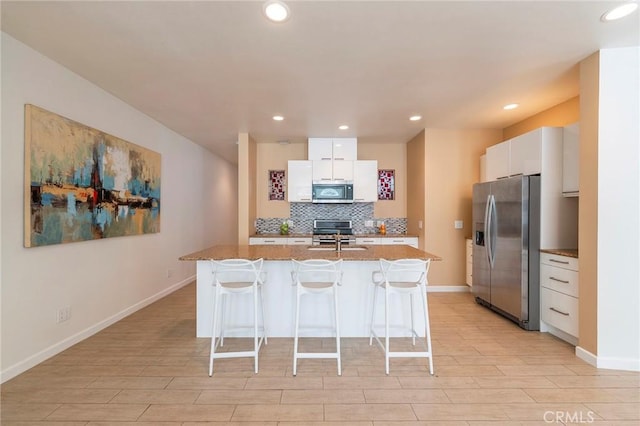 kitchen featuring white cabinetry, backsplash, a kitchen bar, a center island with sink, and appliances with stainless steel finishes