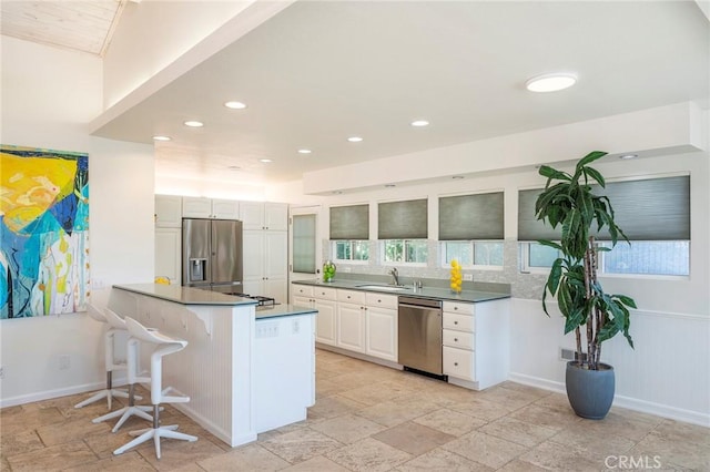 kitchen with kitchen peninsula, appliances with stainless steel finishes, sink, white cabinets, and a breakfast bar area