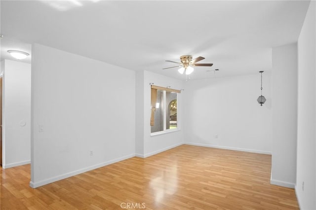 spare room with a ceiling fan, light wood-type flooring, and baseboards