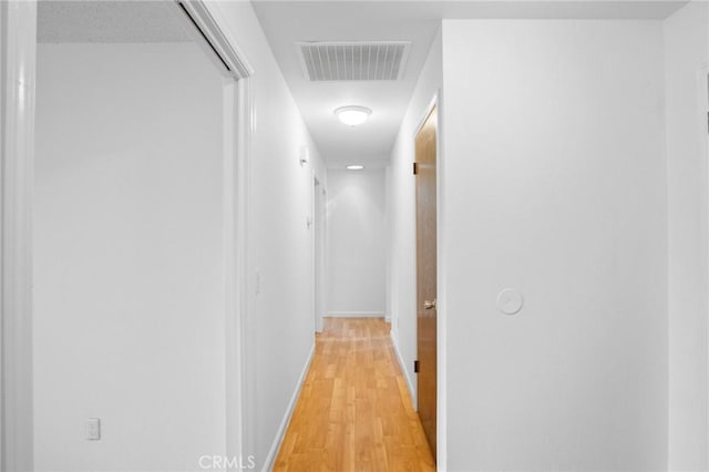 hallway with light wood finished floors, visible vents, and baseboards