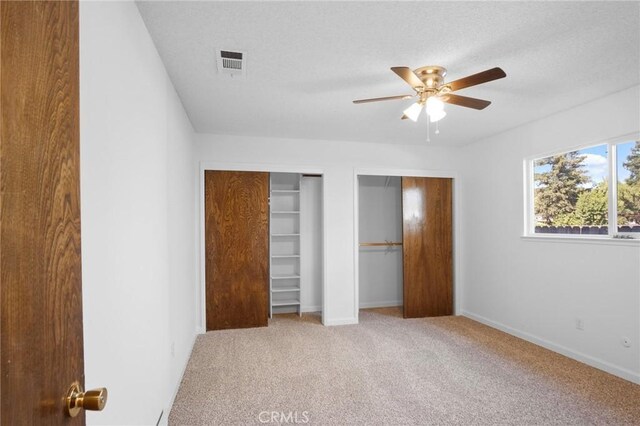 unfurnished bedroom with ceiling fan, two closets, light colored carpet, and a textured ceiling