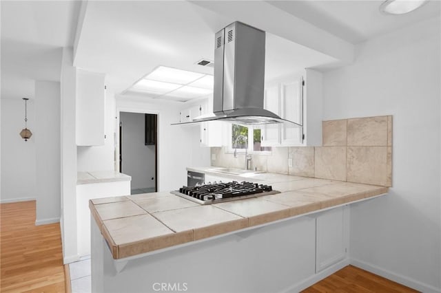 kitchen featuring island range hood, backsplash, a peninsula, stainless steel gas cooktop, and a sink