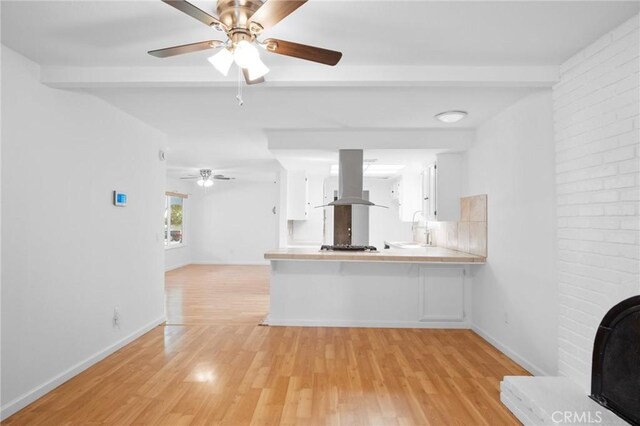 kitchen with island range hood, light wood-type flooring, ceiling fan, sink, and kitchen peninsula