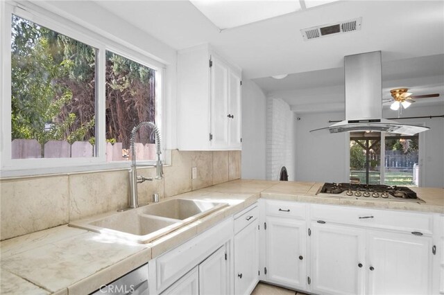 kitchen featuring island exhaust hood, backsplash, ceiling fan, sink, and stainless steel gas cooktop