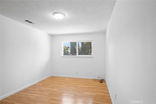 unfurnished room with baseboards, a textured ceiling, visible vents, and light wood-style floors