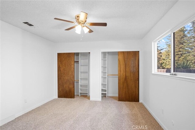 unfurnished bedroom featuring ceiling fan, multiple closets, a textured ceiling, and light carpet