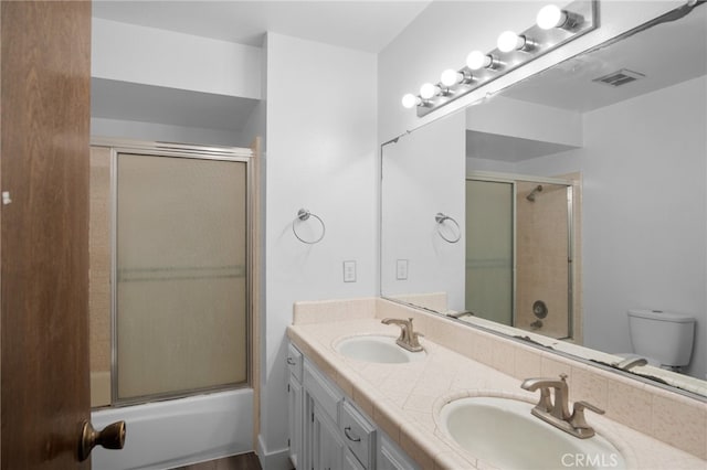 full bathroom featuring double sink vanity, toilet, and enclosed tub / shower combo