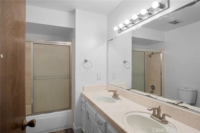 full bath featuring double vanity, combined bath / shower with glass door, a sink, and visible vents