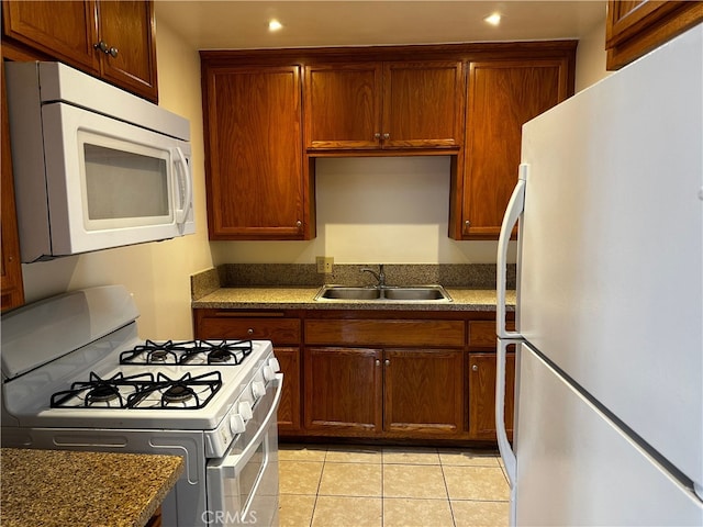 kitchen with sink, dark stone counters, white appliances, and light tile patterned floors