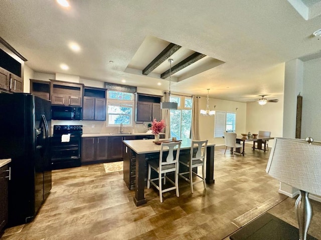 kitchen with ceiling fan with notable chandelier, black appliances, a kitchen island, a kitchen bar, and sink