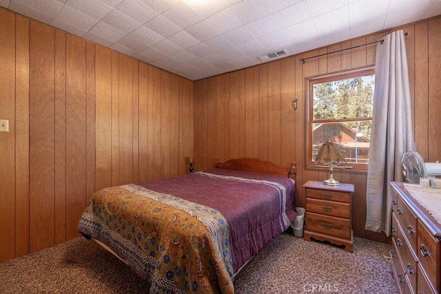 bedroom with light carpet, visible vents, and wooden walls