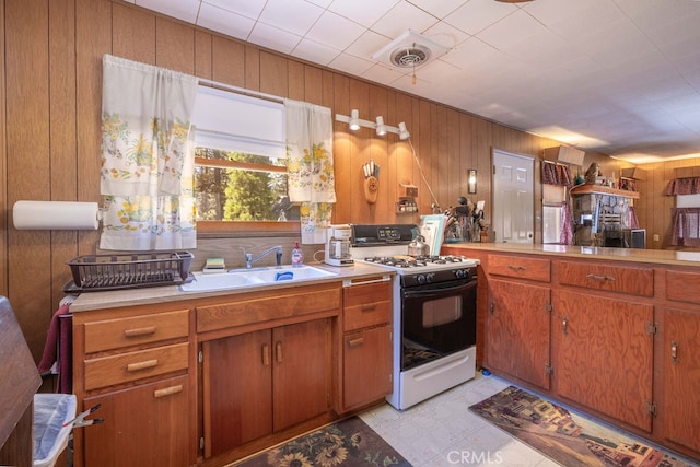 kitchen featuring wood walls, sink, light tile patterned floors, and white gas stove