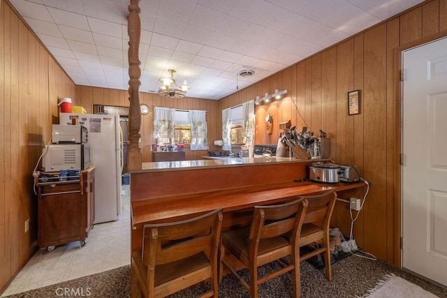 bar featuring light floors, visible vents, an inviting chandelier, freestanding refrigerator, and wood walls